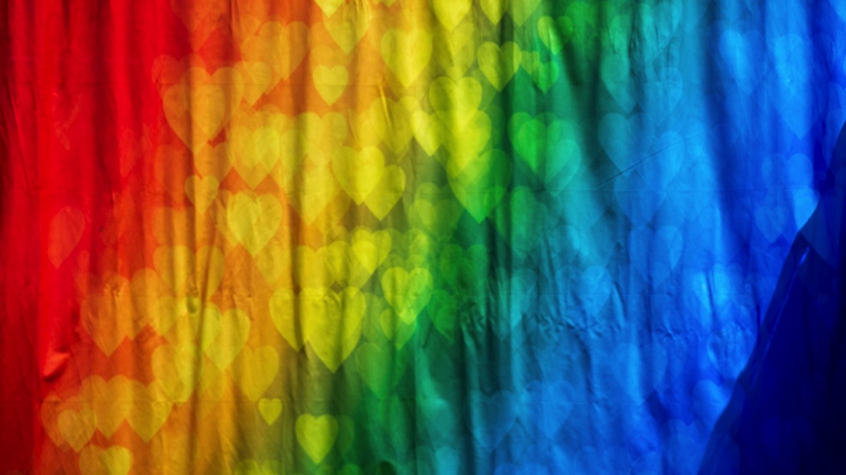 A piece of fabric with the colors of the rainbow with hearts of matching colors and of varying sizes and opacity superimposed over the fabric.